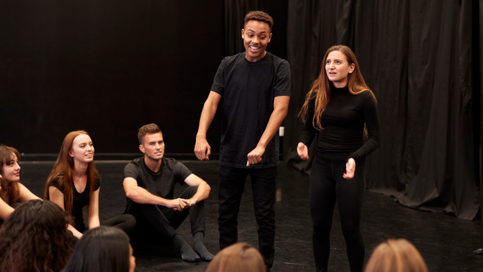 Teen improvisers performing a scene while their class watches
